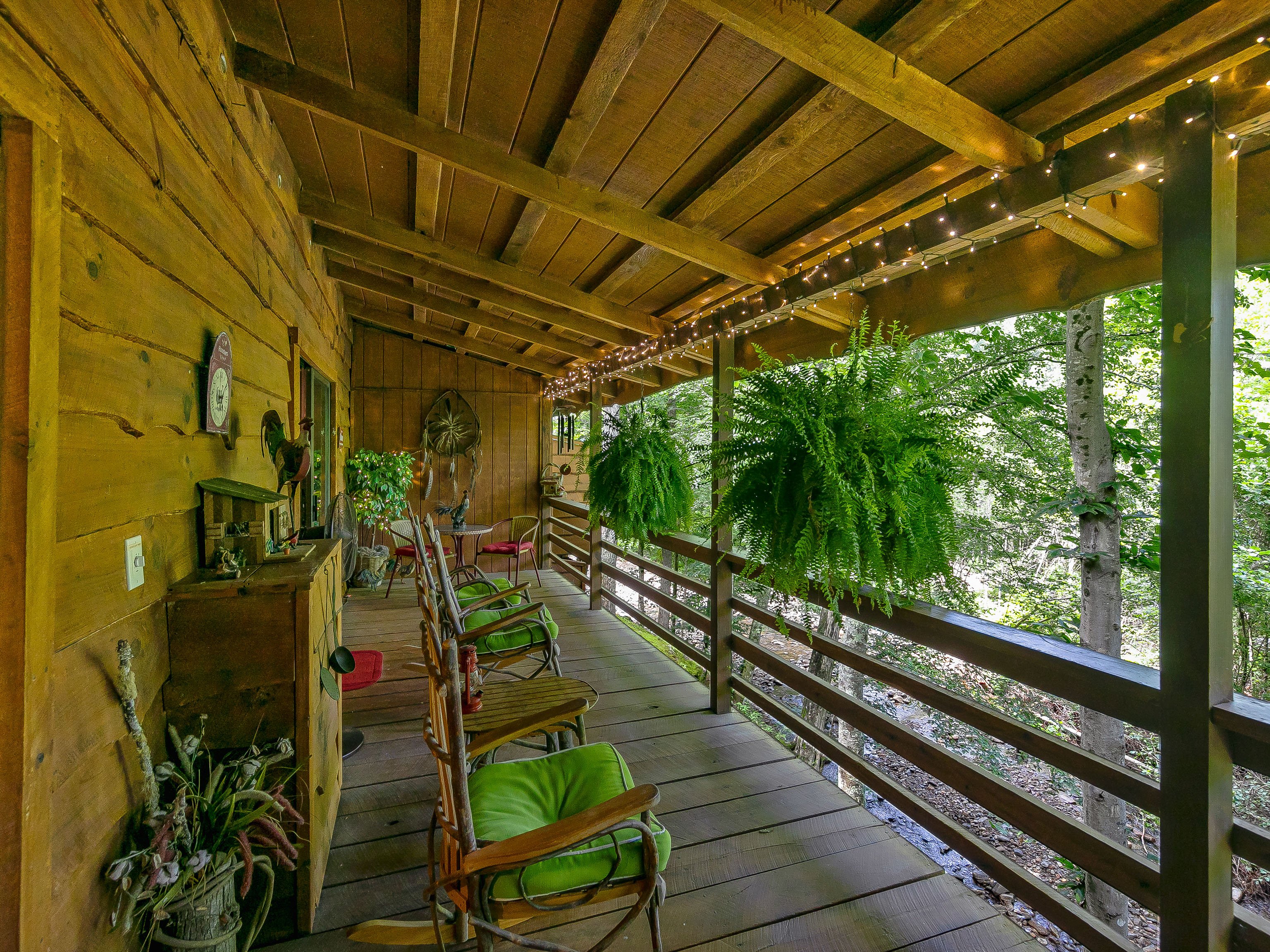 Creekside porch with rocking chairs, ferns, and string lights